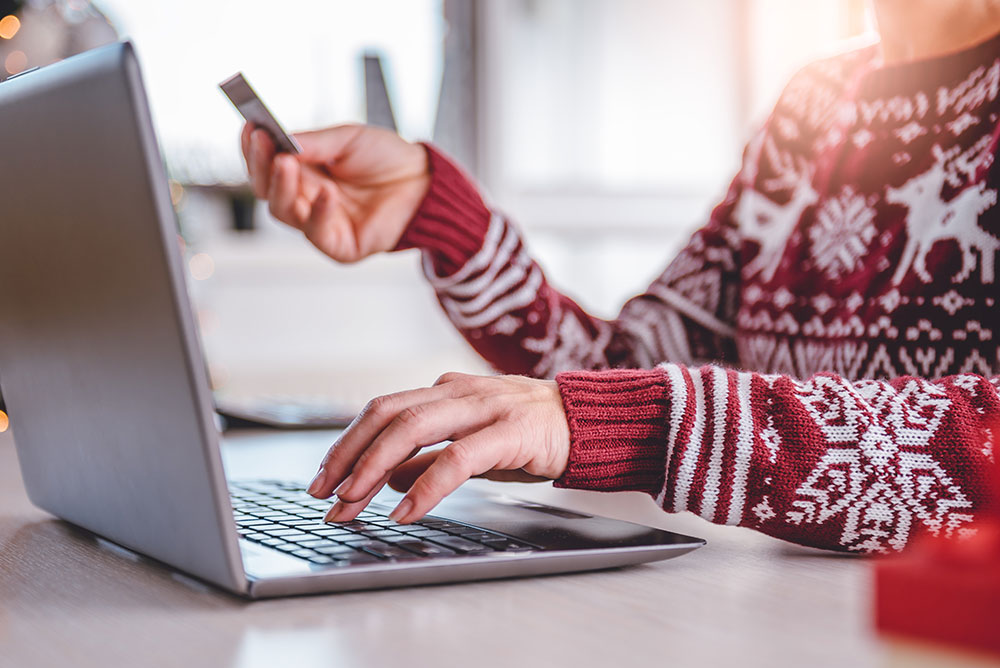 Person wearing a festive sweater uses a laptop